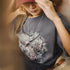 Person wearing a t-shirt with a bear and eagle design, holding a red hat.